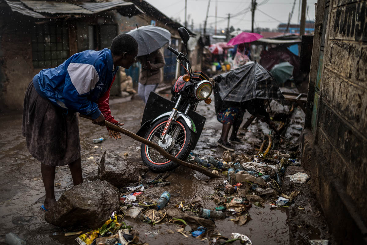 A group of women clean the open sewer that runs in front of their residential compound in the Soweto area of Kibera, trying to prevent the rainwater and rubbish from flowing inside their homes. [Brian Otieno/Al Jazeera]