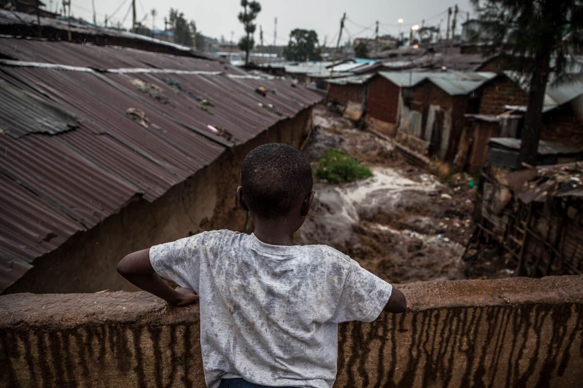 A child watches the brown waters of the river rising with the rainfall from atop a bridge in the Lindi area of Kibera. With the arrival of the rains, the river becomes a roiling torrent that carries sewage and all forms of waste downstream. [Natalia Jidovanu/Al Jazeera]