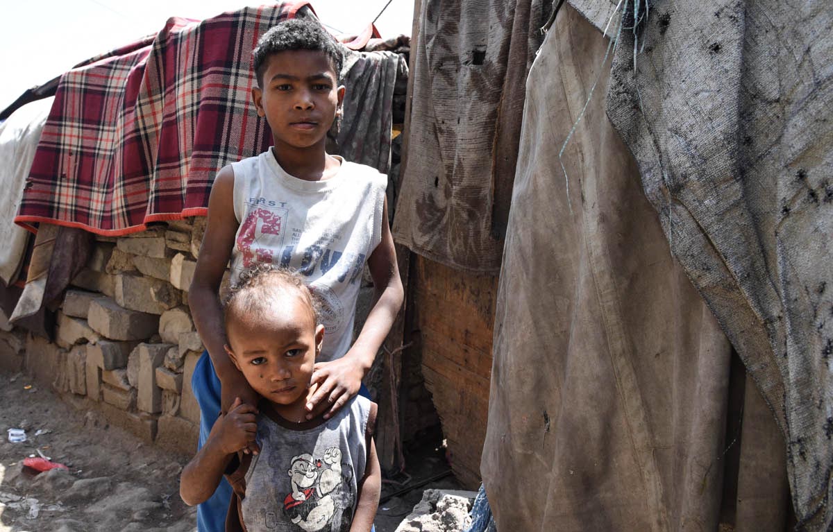 Abdullah, 8, and his brother Hussein, 2, in front of their shelter in a camp for displaced people in Sana'a city. Abdullah joins his father each day as they try to eke out a living in their new surroundings. 'I spend my days collecting plastic jerry cans for water. Every morning I collect them and try to sell them,' says Abdullah. [Becky Bakr Abdulla/Norwegian Refugee Council]