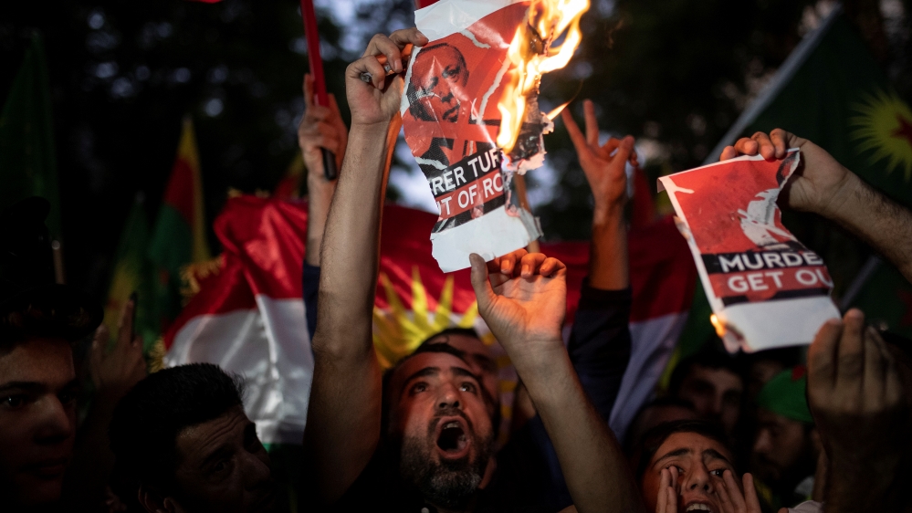 Kurds living in Greece shout slogans while burning a poster depicting Turkish President Tayyip Erdogan during a demonstration against Turkey's military action in northeastern Syria, in Athens