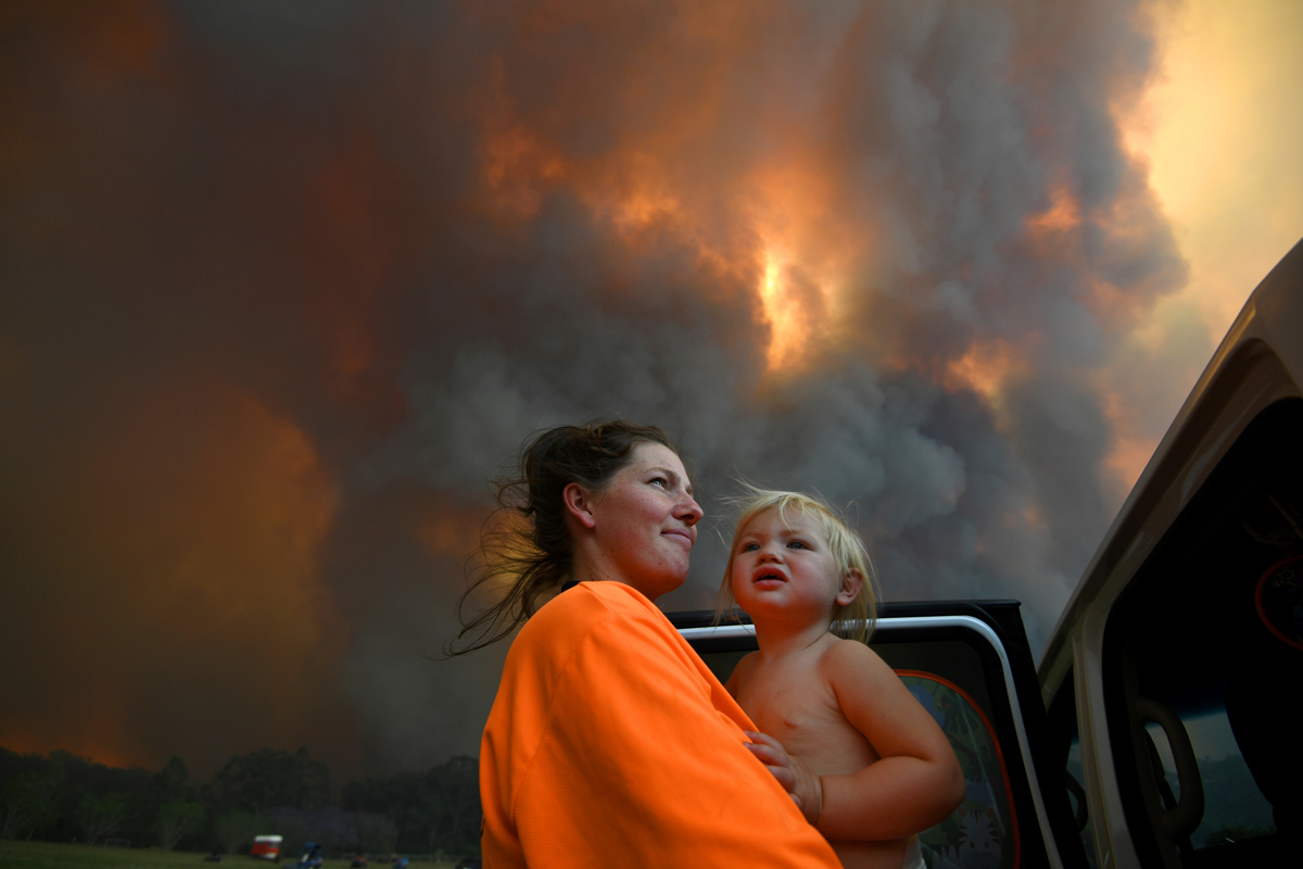 Sharnie Moren and her 18-month-old daughter Charlotte look on as thick smoke rises from the fires near Nana Glen, Coffs Harbour. [Dan Peled/AAP Image via Reuters]