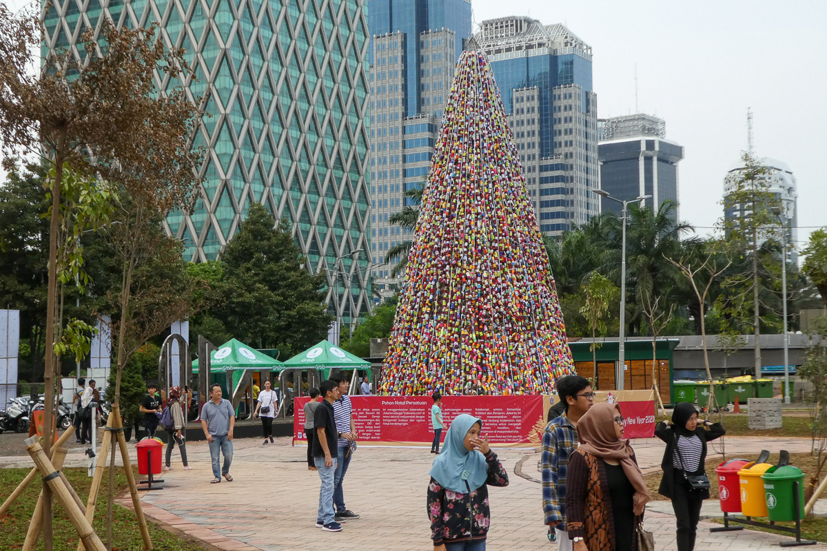 Indonesians walk by a Christmas tree made with used plastic bottles covered with fabric in Jakarta. [Bay Ismoyo/AFP]
