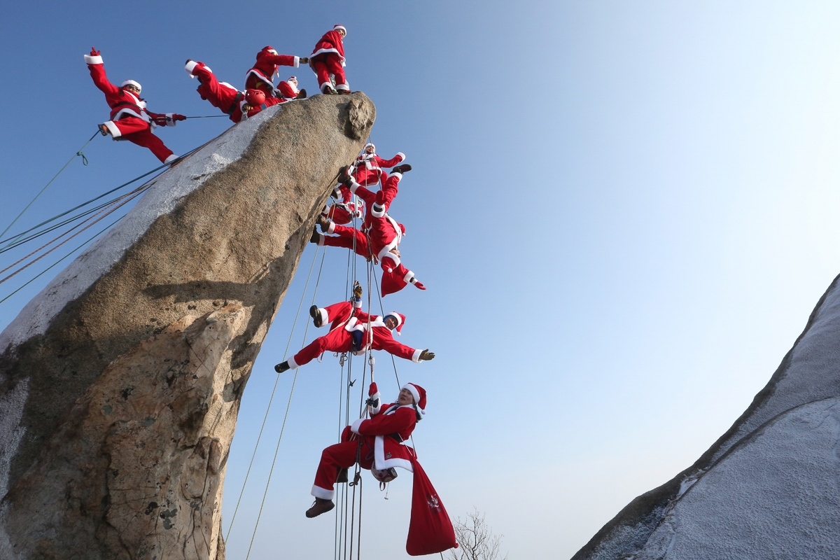 Mountain climbers in Santa outfits pose during an event to encourage safe climbing and promote Christmas charity on the Buckhan mountain in Seoul, South Korea. [Ahn Young-joon/AP Photo]