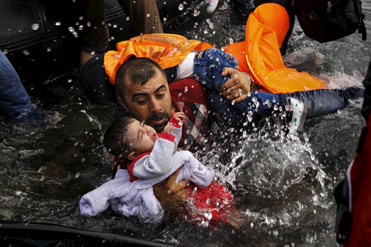 A Syrian refugee holds onto his children as he struggles to walk off a dinghy on the Greek island of Lesbos, after crossing a part of the Aegean Sea from Turkey, September 24, 2015. Yannis Behrakis, the photographer behind this image, spent his final years documenting the refugee crisis before he died in March 2019. [Yannis Behrakis/Reuters]