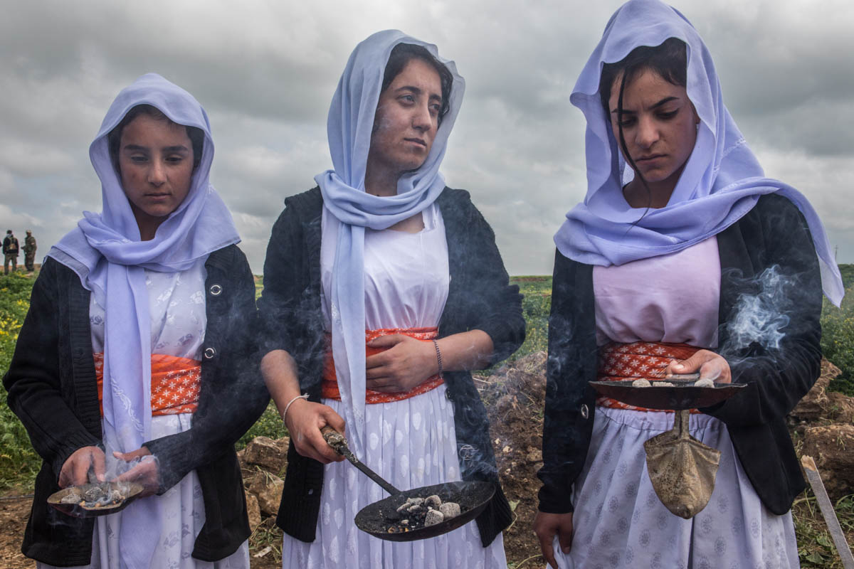 Three Yazidi women burn incense during the ceremony for the opening of the first mass grave in Kojo, Sinjar on March 15. The Iraqi team of Legal Medicine and Mass Graves Department together with the UN investigative team started to work on Yazidi mass graves on the same day. [Alessio Mamo/Al Jazeera]