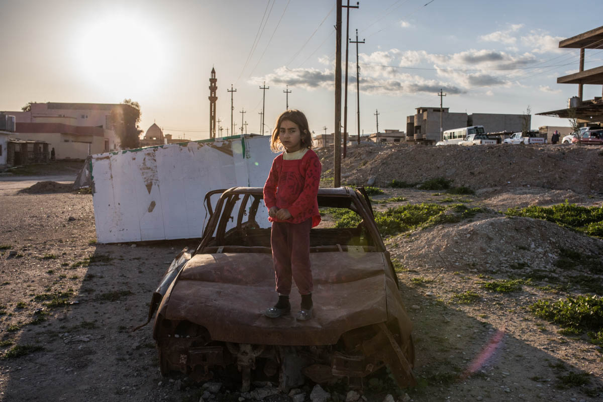 A Yazidi girl playing above an abandoned car in the city of Sinjar. Many of the displaced people who escaped and survived ISIL came back to their city, living often in poor conditions in the heavily damaged city. [Alessio Mamo/Al Jazeera]
