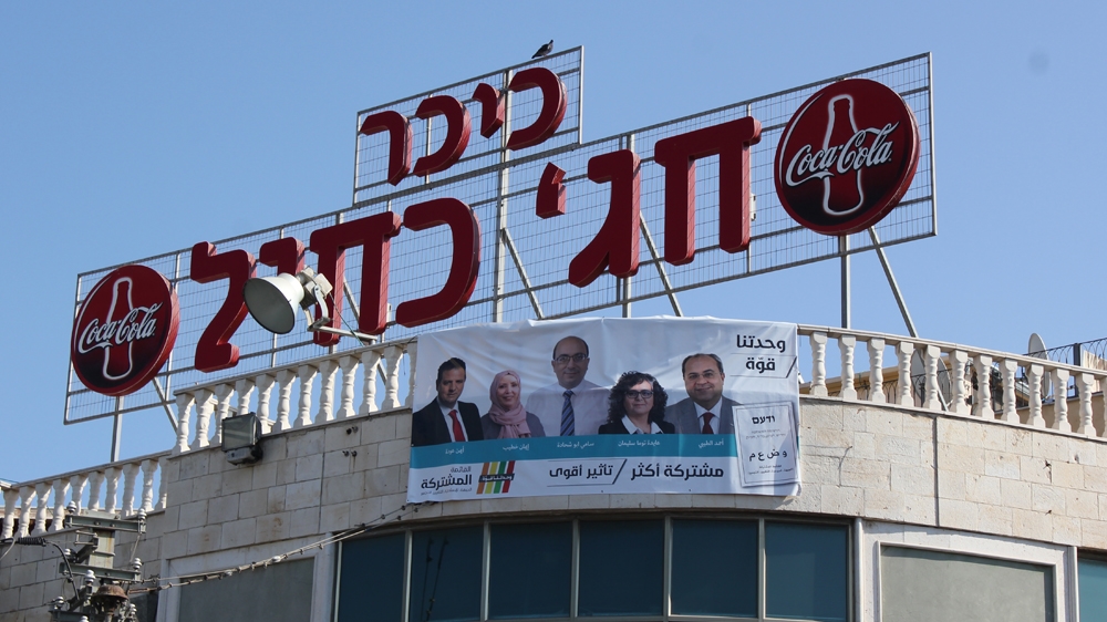 Campaign posters plastered across buildings and shop windows in Jaffa ahead of next week's election. [Arwa Ibrahim/ Al Jazeera]
