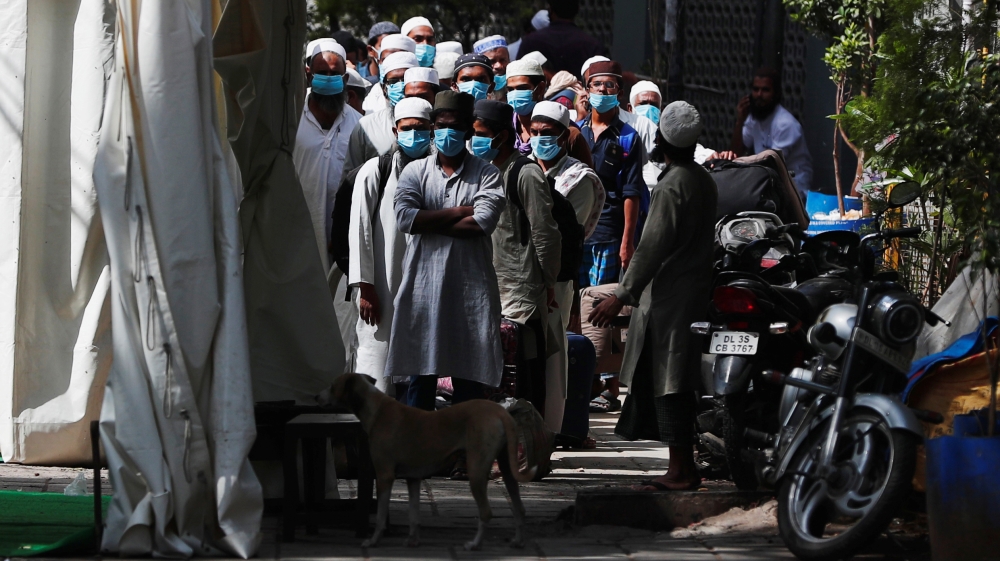 Men wearing protective masks wait for a bus that will take them to a quarantine facility, amid concerns about the spread of coronavirus disease (COVID-19), in Nizamuddin area of New Delhi