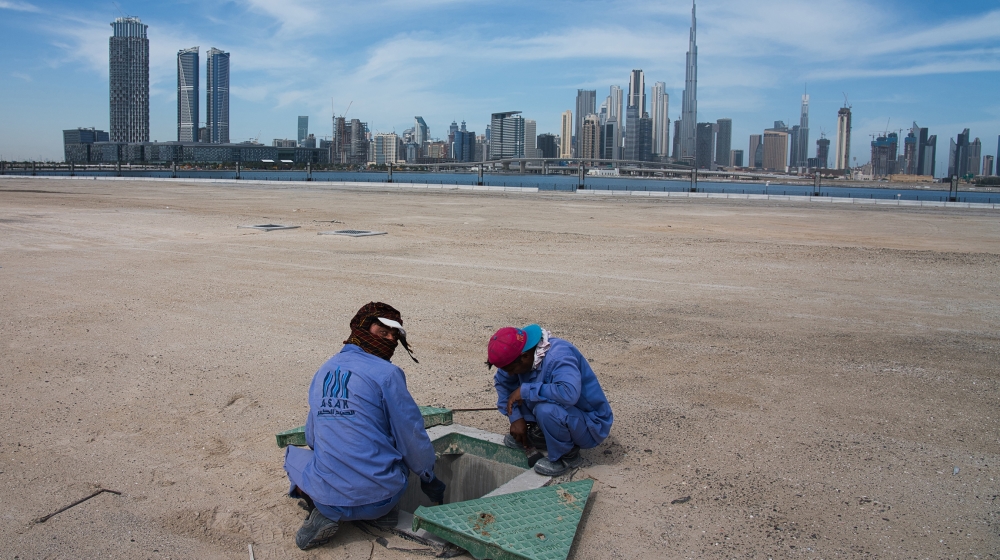 Two construction workers examine a drainage system with the Burj Khalifa, the world's tallest building, in the skyline behind them in Dubai, United Arab Emirates, Monday, April 6, 2020. Dubai, one of 