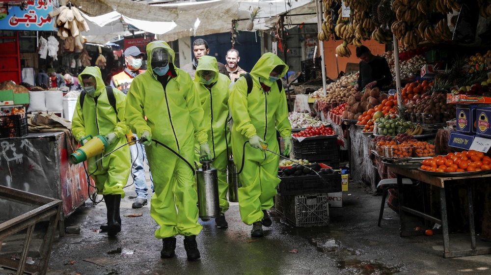 Trabajadores que usan desinfectante en aerosol de equipo de protección como precaución contra el coronavirus, en el mercado principal de la ciudad de Gaza, el viernes 27 de marzo de 2020. El municipio de Gaza cierra todo el viernes semanal