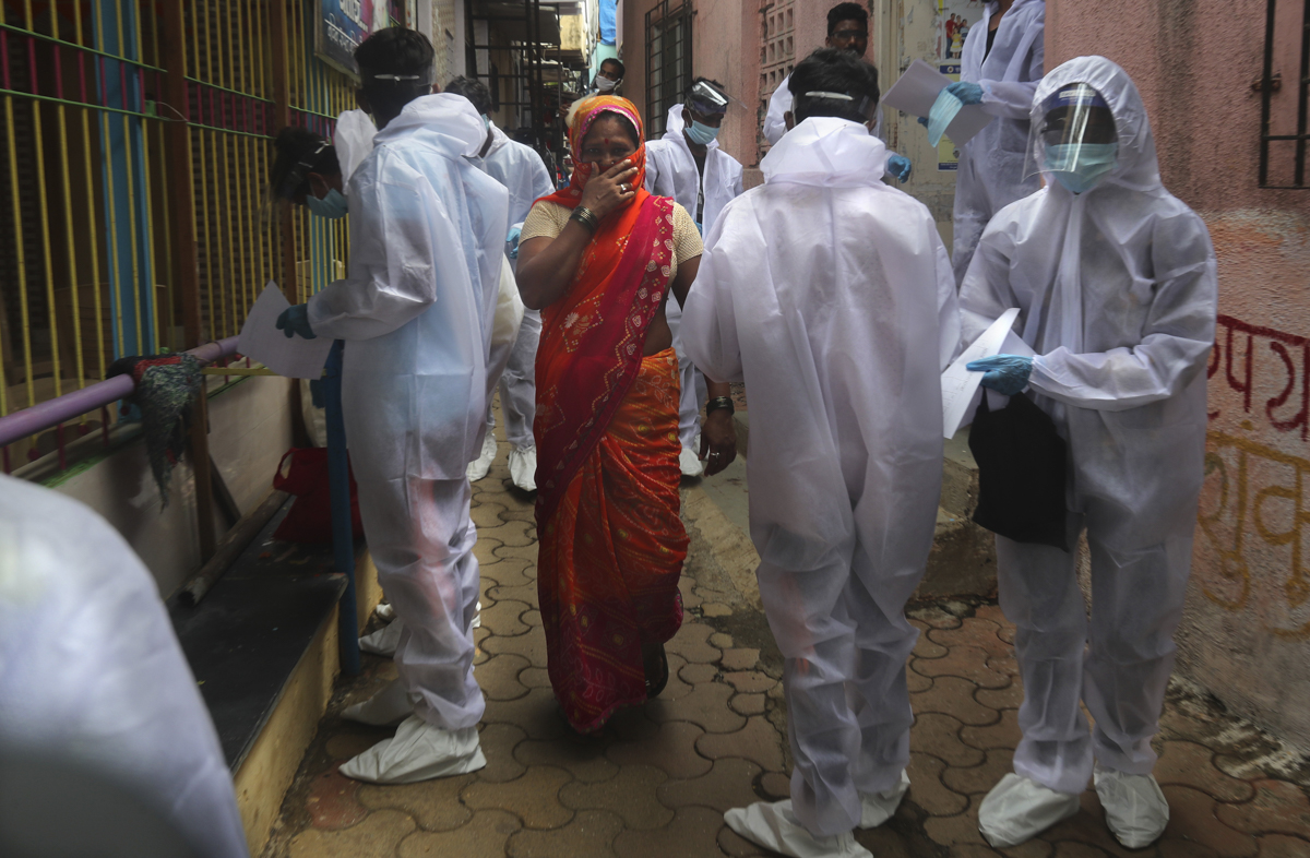A woman covers her face as she walks past healthcare workers arriving to administer free medical check-ups in a slum in Mumbai. [Rafiq Maqbool/AP Photo]