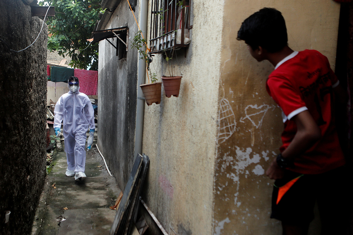 A healthcare worker walks in an alley of a slum during a check-up for the coronavirus disease in Mumbai. [Francis Mascarenhas/Reuters]