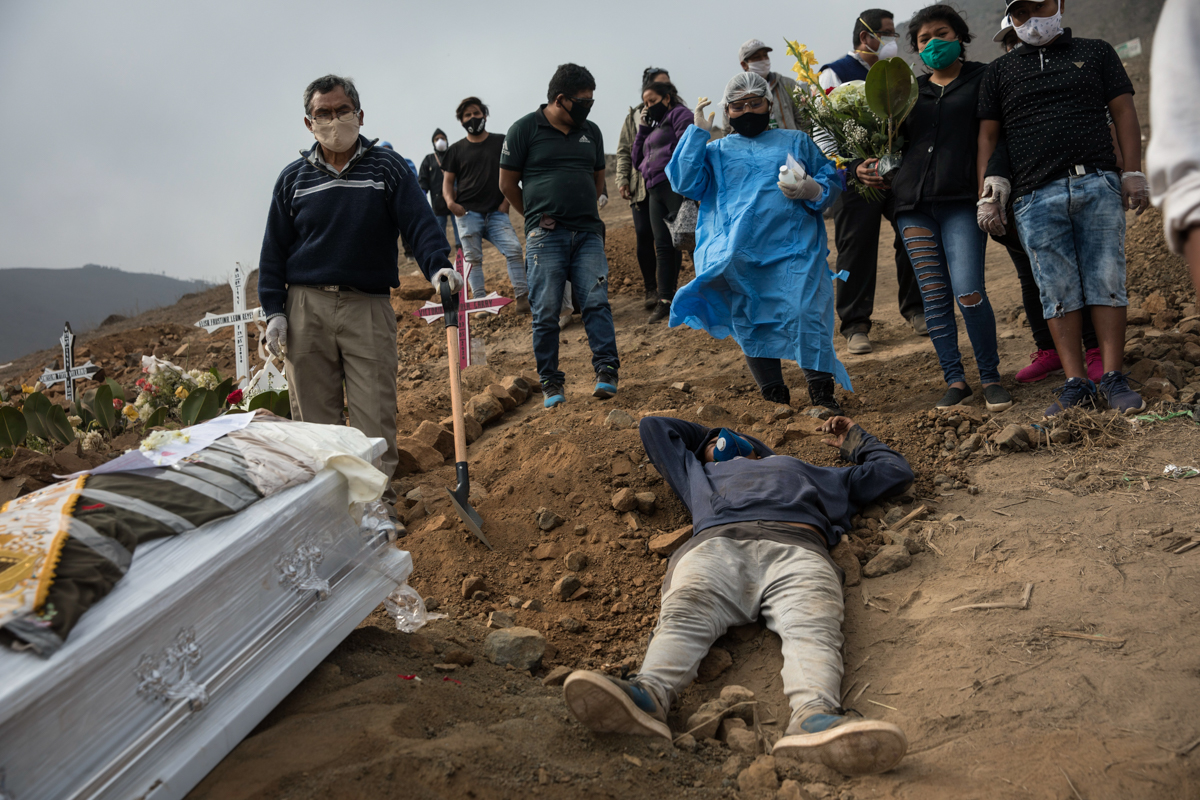 An exhausted cemetery worker lies on the ground after carrying the coffin of Victor Gaspar up the hill at the Nueva Esperanza cemetery. [Rodrigo Abd/AP Photo]