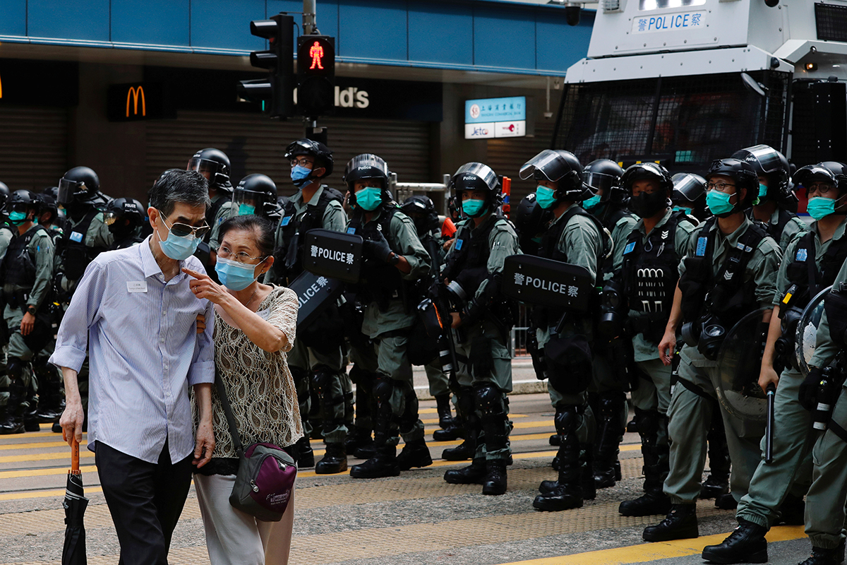 A couple walks past riot police as anti-national security law protesters march during the anniversary of Hong Kong's handover to China from Britain. [Tyrone Siu/Reuters]