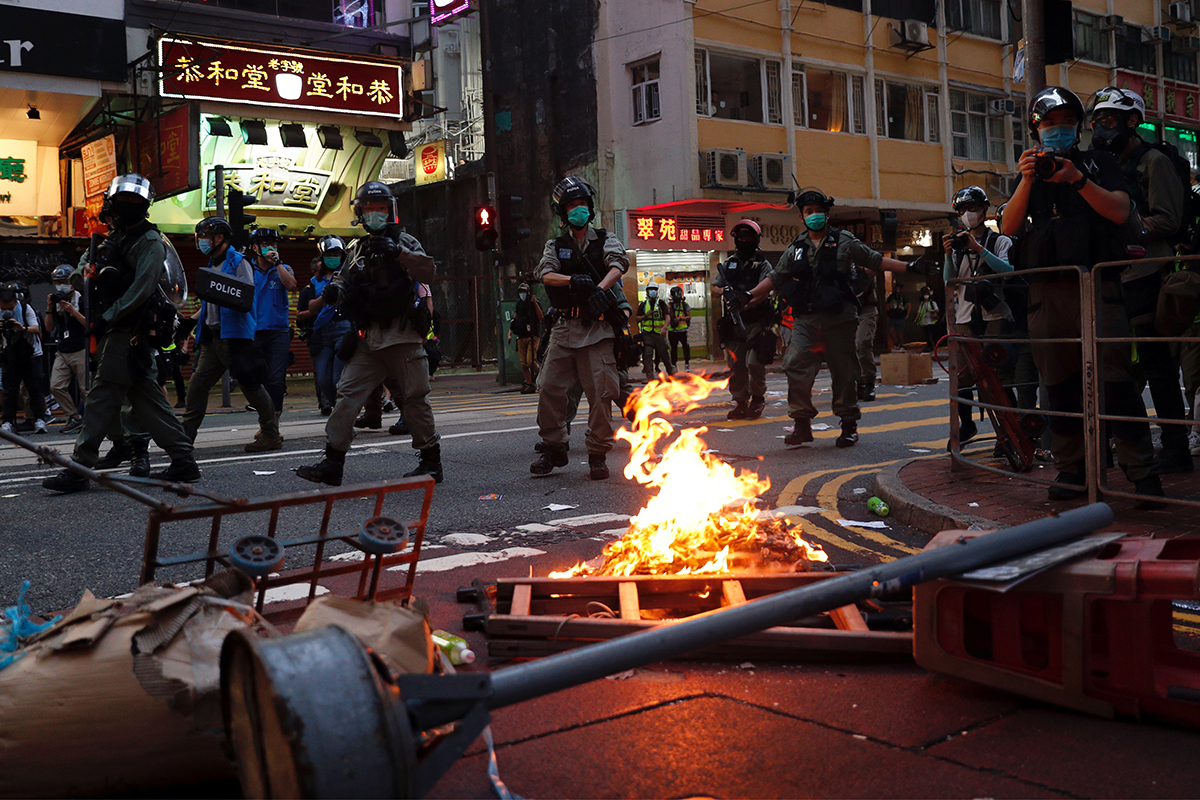 Riot police walk past a fire set by anti-national security law protesters during the march. [Tyrone Siu/Reuters]