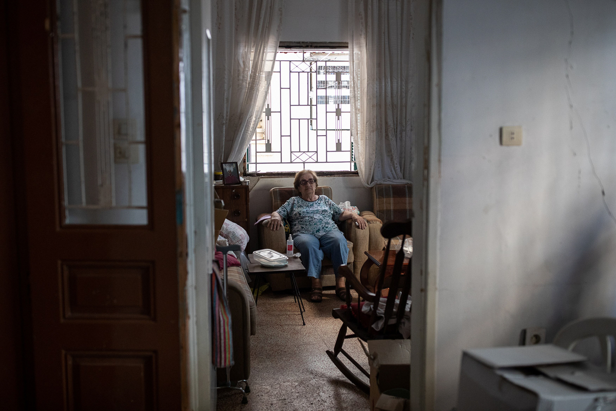 Marguerite Dirany, 81, sits in the living room of her damaged home. [Alkis Konstantinidis/Reuters]