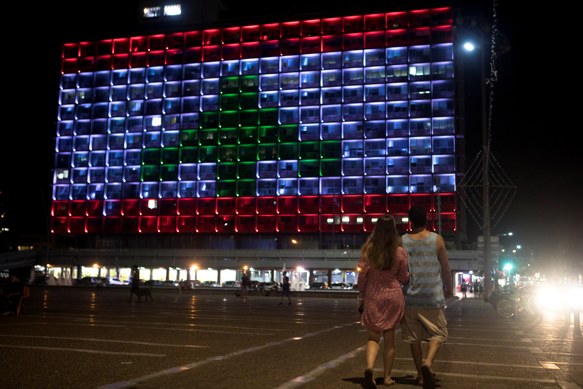 A couple walks in Rabin square in Tel Aviv, Israel, as the municipality building is lit in the colours of the Lebanese flag, in a rare show of Israeli solidarity with Beirut as it reels from the devastating explosion. [Nir Elias/Reuters]