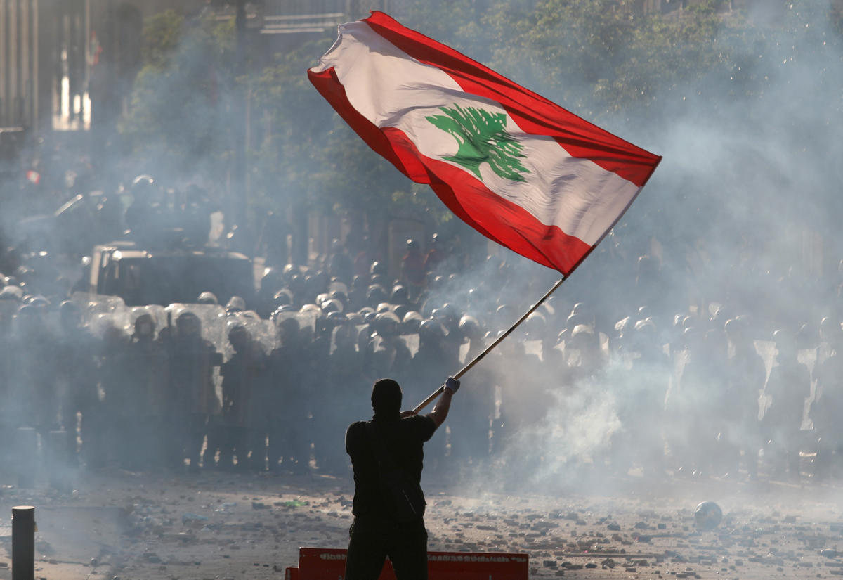 A demonstrator waves the Lebanese flag in front of riot police. [Goran Tomasevic/Reuters]