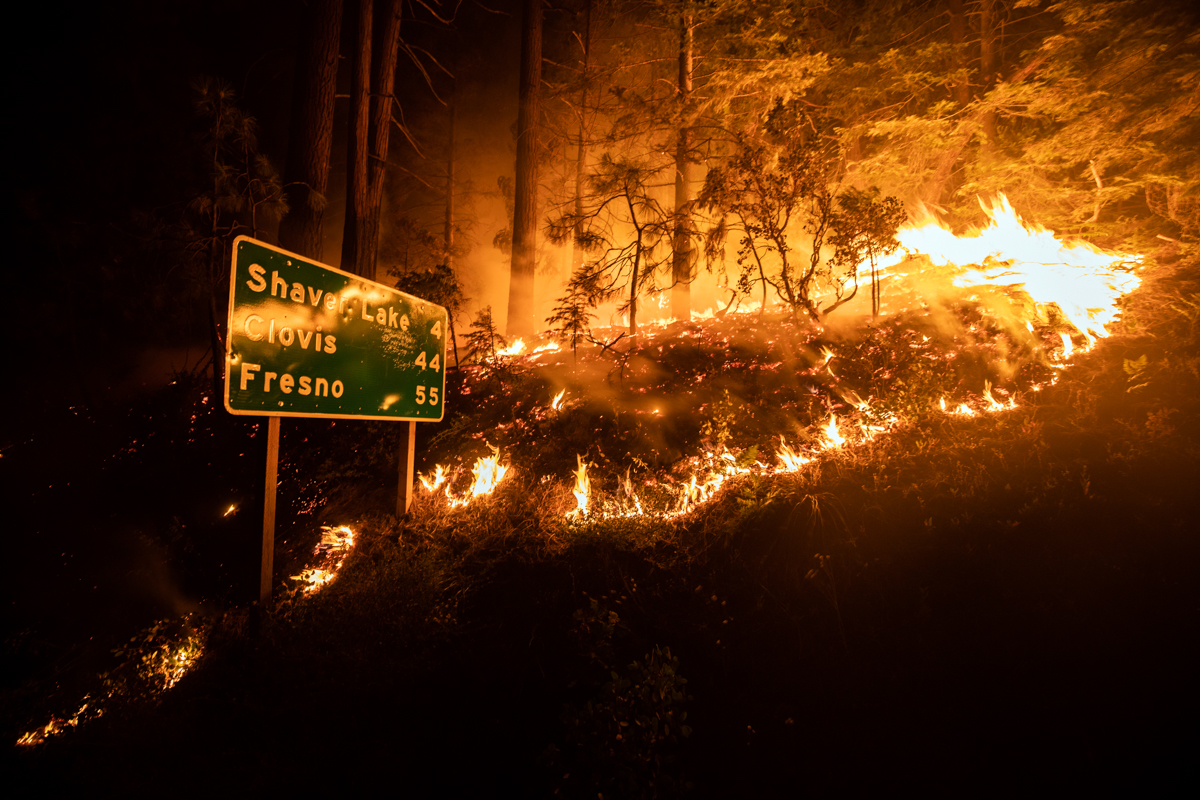 The Creek Fire burns next to a traffic sign giving the direction of Shaver Lake, Clovis and Fresno near Shaver Lake in the Sierra National Forest. [Etienne Laurent/EPA]