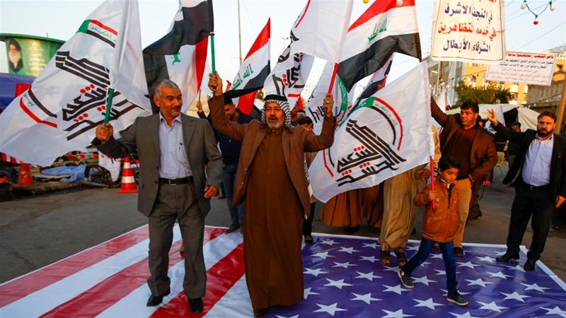 Iraqi people walk on a United States flag in a protest after an air attack at the headquarters of Kataib Hezbollah militia group in al-Qaim, Iraq [Alaa al-Marjani/Reuters]