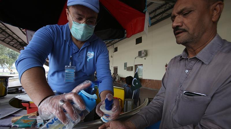 A volunteer helps a passenger arriving at a railway station to clean his hands to help prevent the spread of coronavirus in Peshawar [Muhammad Sajjad/AP Photo]