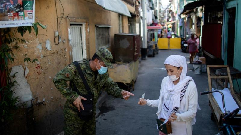 A soldier wearing a protective mask checks a woman's quarantine pass in Manila as part of imposed movement restrictions. President Rodrigo Duterte is expected to decide on whether to extend the lockdown on Thursday [Eloisa Lopez/Reuters]