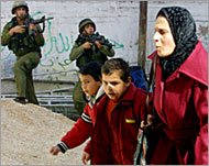 A woman and her children walkpast soldiers in Balata camp
