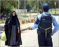 A woman walks past a police officer during a curfew in Baquba