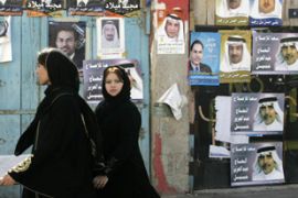 Bahraini women walk past posters of candidates running in Bahrain's upcoming parliamentary elections,