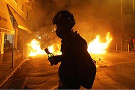 A protestor carries a molotov coctail by a burning barricade in the center of Athens