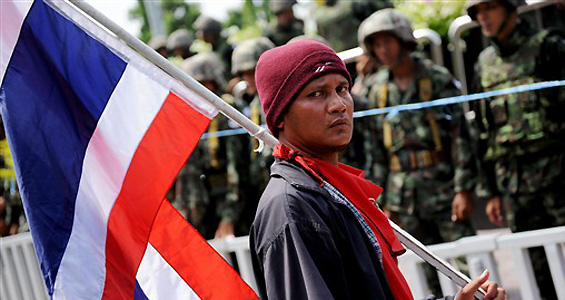 THAILAND, PATTAYA : A protester loyal to fugitive ex-PM Thaksin Shinawatra parades a national flag outside the venue of the 14th Association of Southeast Asian Nations (ASEAN) Summit and Related Summits as soldiers stand guard, in Pattaya some 180 km south-east of Bangkok on April 11, 2009. Thai anti-government demonstrators blockaded a summit of Asian leaders for a second day, forcing the postponement of two key meetings, with reports of three people injured. AFP PHOTO/Christophe ARCHAMBAULT