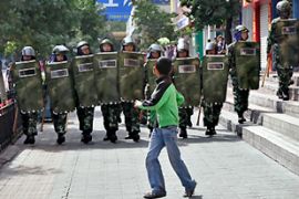 A boy runs in front of a line of Chinese security forces as they clear the crowds after a reported syringe stabbing incident in Urumqi