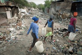 Women walk through a ravine filled with garbage in Haiti