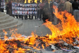 Protestors stand next to leaflets and flags burning near the office of former Kyrgyz president Kurmanbek Bakiyev''s