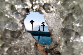 A Tunisian woman, seen through a broken glass window, walks next to the swimming pool at the empty and ransacked home of Kaif Ben Ali, nephew of former President Zine al-Abidine Ben Ali, in Hammamet