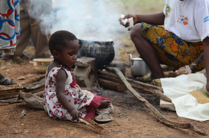 Girl sits next to her mother while she prepares meal in refugee camp in Grand Gedah county