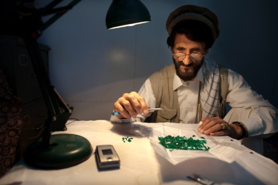 Afghan man studying uncut emeralds with tweezers under a light