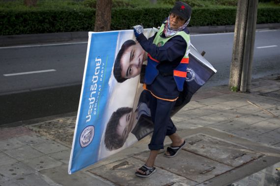 Sunwin, a street sweeper, sets aside a Democrat Party campaign poster showcasing an image of Prime Minister Abhisit Vejjajiva