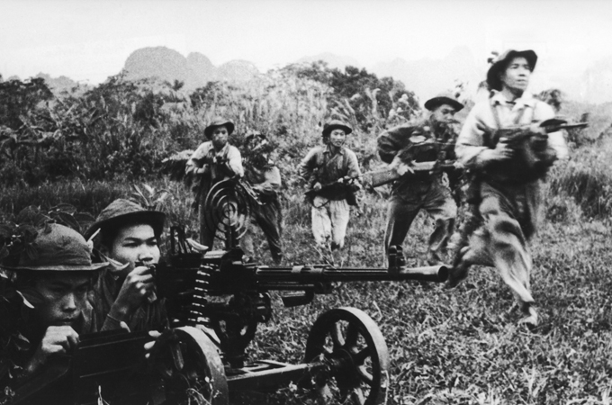 Vietnamese communist soldiers moving forward under covering fire from a heavy machine gun during the Vietnam War.