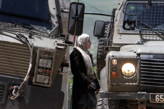 A Palestinian woman in between two Israeli military SUV