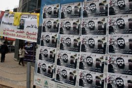 A Palestinian woman walks towards posters of prisoner Khader Adnan