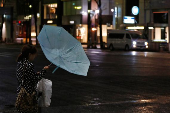 A woman struggles with strong winds and rain caused by Typhoon Jelawat