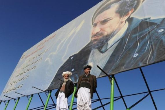 Afghan men stand in front of a giant pos