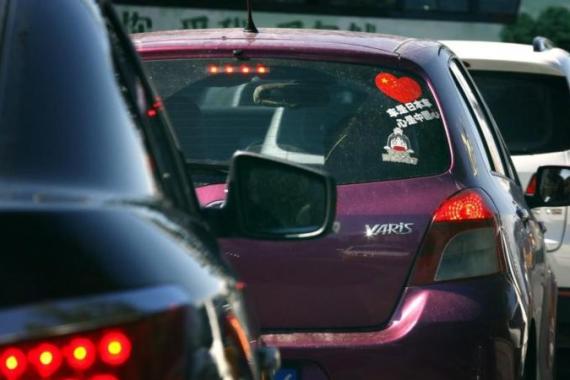 The driver of a Toyota Yaris car is reflected in a mirror as he drives along a main road in central Beijing