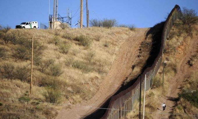 A woman walks near the border fence between Mexico and the U.S. in Nogales, as a border patrol vehicle is parked on the U.S. side of the border