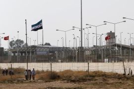 Syrian men, with the damaged Syrian Tel Abyad custom office in the background, walks from Syria to Turkey after crossing the fences next to the Akcakale border gate