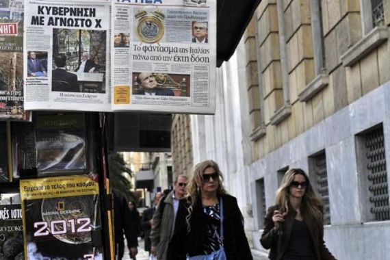 Women walk by Greek newspapers displayed