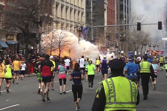 Runners continue to run towards the finish line as an explosion erupts at the finish line of the Boston Marathon