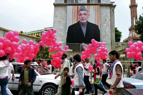 Afghan volunteers walk past a poster of Afghan President Hamid Karzai