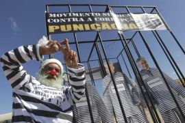 A man poses with cutouts of politicians dressed as prisoners in a cage as he protests against corruption in front of the Supreme Court during the